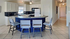 A modern kitchen with white cabinets, a blue island, and three bar stools. - Here Comes the Sun by Ryson Vacation Rentals (Galveston)