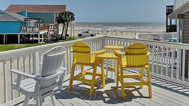 Een terras met witte en gele Adirondack-stoelen, een klein tafeltje en uitzicht op de oceaan.
