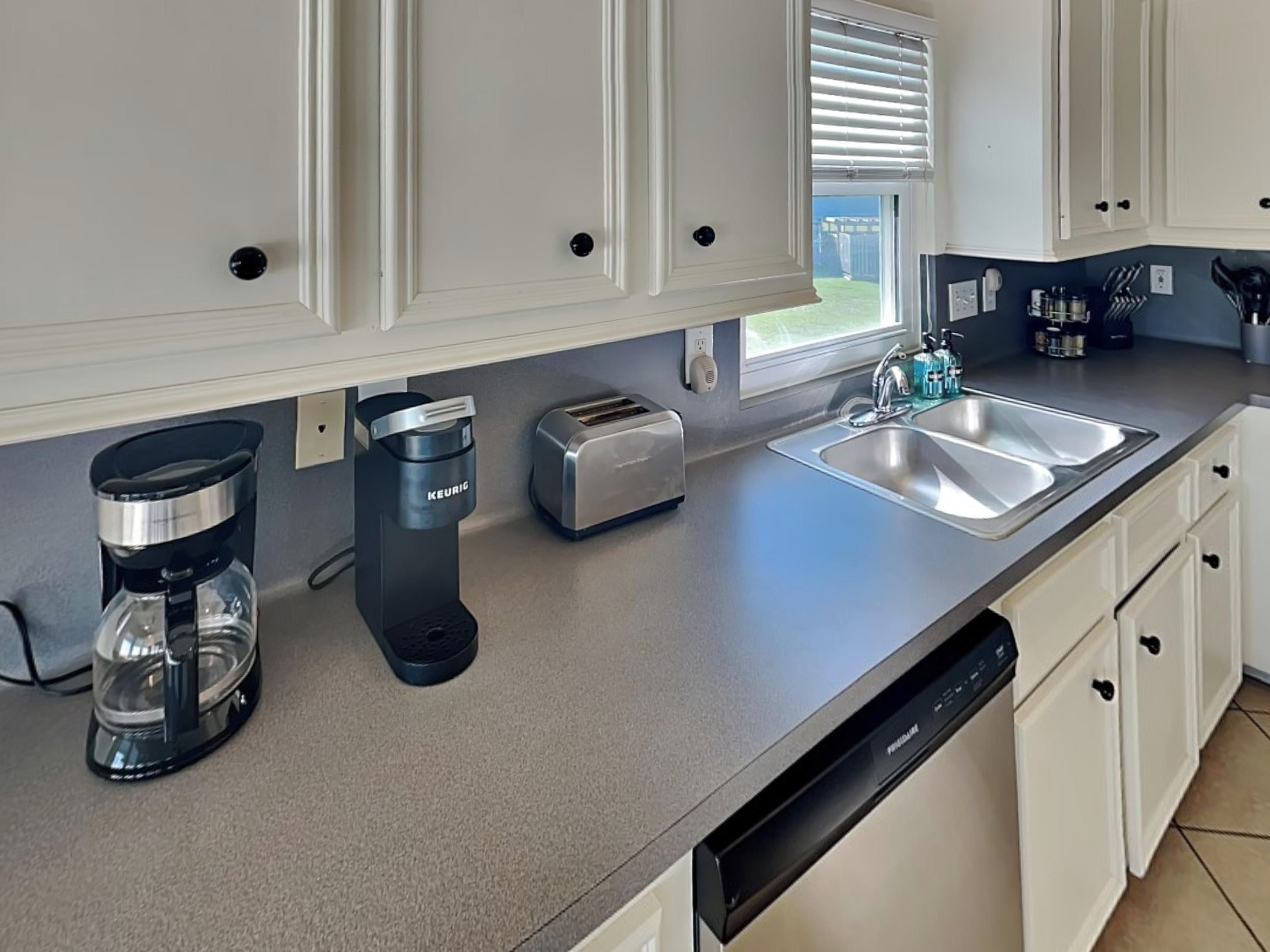 A modern kitchen with white cabinets, a stainless steel sink, a toaster, and a coffee maker.