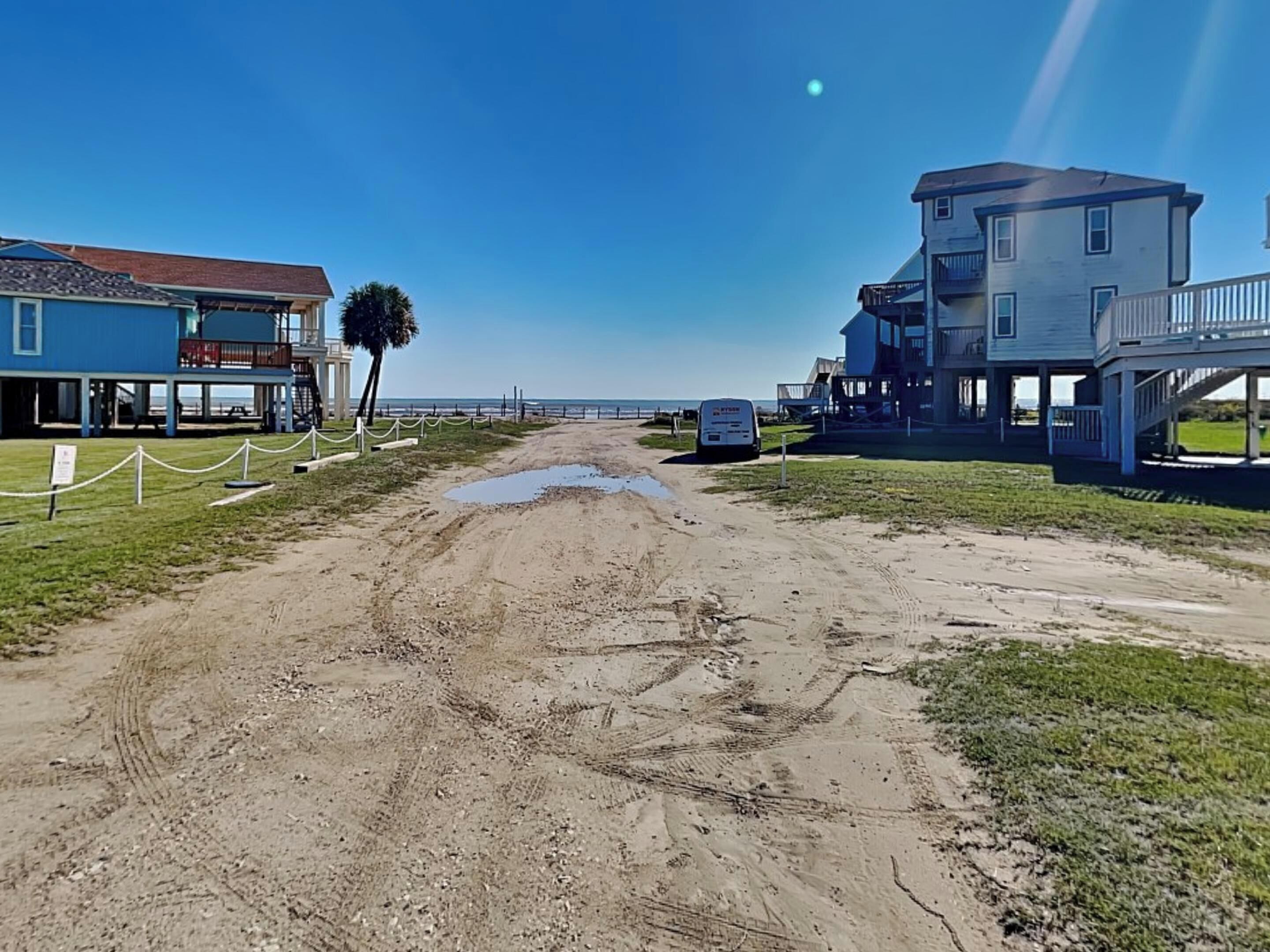 A beachside road leading to a building with a balcony and a signboard.