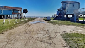 Een weg langs het strand die leidt naar een gebouw met een balkon en een bord.