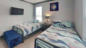 A bedroom with two beds, a TV, a window, and a painting. - Honu Beachfront by Ryson Vacation Rentals (Galveston)