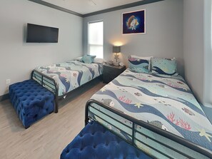 A bedroom with two beds, a TV, a window, and a painting. - Honu Beachfront by Ryson Vacation Rentals (Galveston)