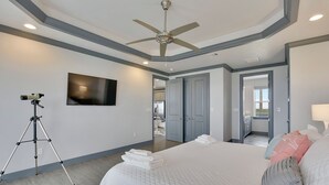 Een slaapkamer met een groot bed, een plafondventilator, een tv aan de muur en een statief.