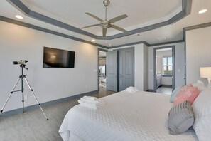 Ein Schlafzimmer mit einem großen Bett, einem Deckenventilator, einem Wand-Fernseher und einem Stativ.