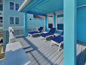 A blue porch with two white lounge chairs and a small table.