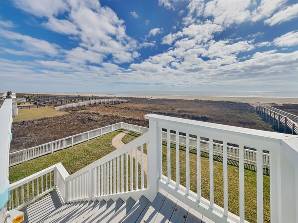 A balcony with a view of a beach and dunes.