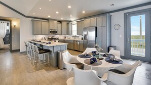 Een moderne keuken met een centraal eiland, roestvrijstalen apparatuur en een eethoek met witte stoelen en een ronde tafel.