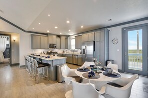 A modern kitchen with a central island, stainless steel appliances, and a dining area with white chairs and a round table.