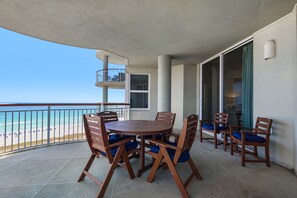 Varanda com mesa e cadeiras, vista para a praia e porta de correr de vidro.