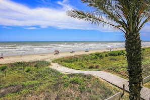 A beach with a wooden boardwalk, palm trees, and people enjoying the seaside.