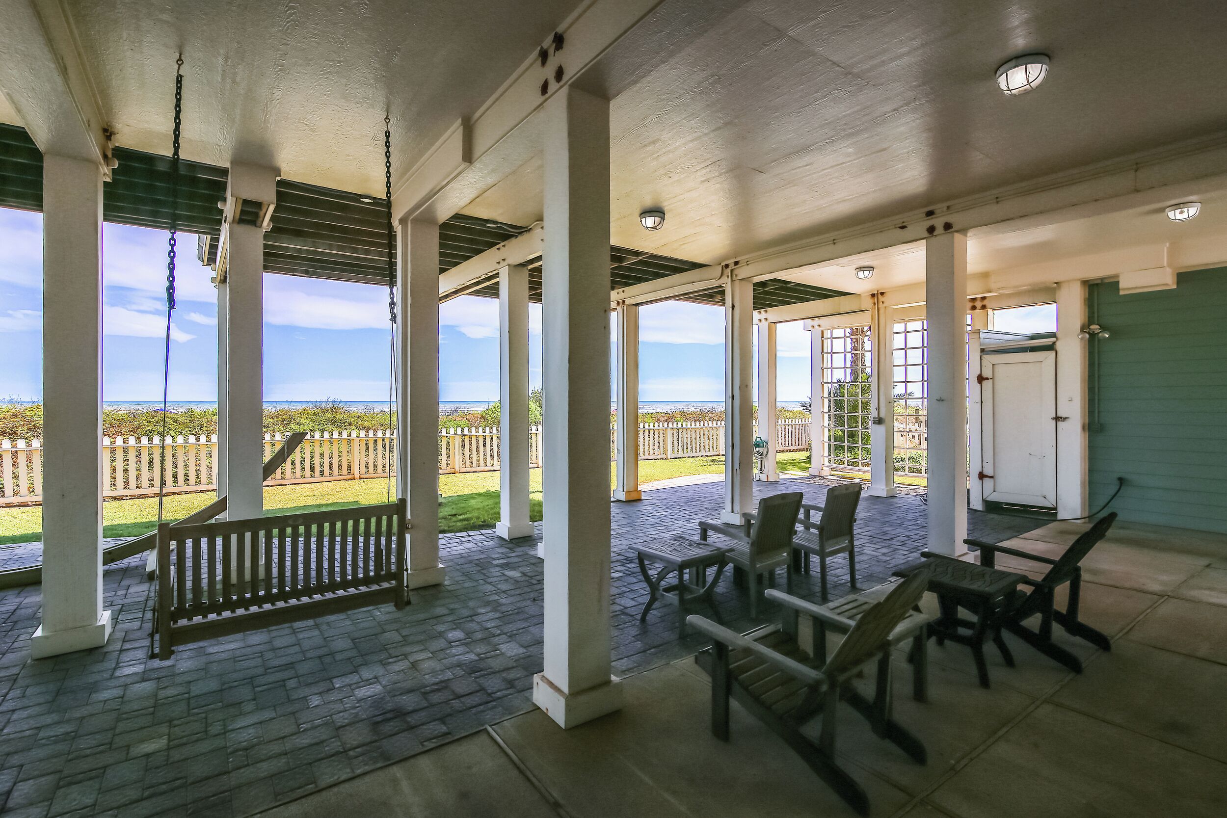 A covered patio with a bench and tables, large windows, and a view of a fence and greenery.