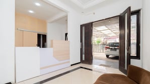 A reception area with a reception desk, a brown sofa, and a view of a parked car outside. - OYO Flagship 90524 Holistay Surabaya New (Surabaya)