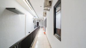 A long, narrow hallway with a black railing on one side, white walls, and a tiled floor. - OYO Flagship 90524 Holistay Surabaya New (Surabaya)