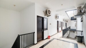 A clean, well-lit hallway with a tiled floor, a black railing, and multiple air conditioning units mounted on the wall. - OYO Flagship 90524 Holistay Surabaya New (Surabaya)