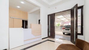 A reception area with a reception desk, a brown sofa, and a view of a parked car outside. - OYO Flagship 90524 Holistay Surabaya New (Surabaya)