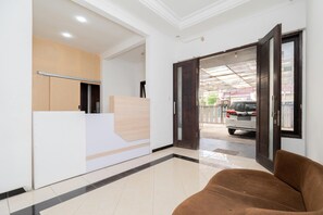 A reception area with a reception desk, a brown sofa, and a view of a parked car outside. - OYO Flagship 90524 Holistay Surabaya New (Surabaya)