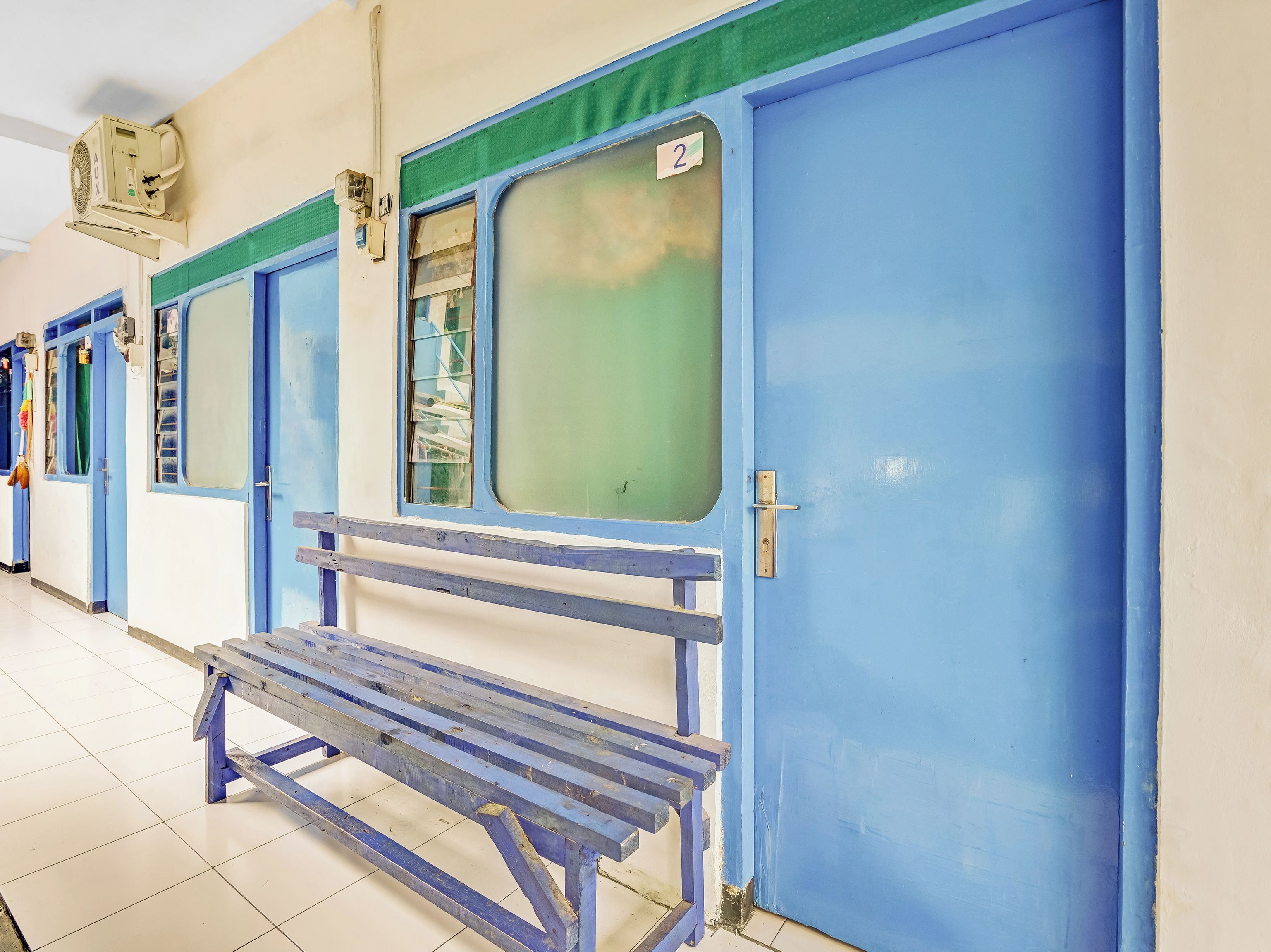 Una fila de puertas azules con un banco delante, un ventilador de techo y piso de baldosas.