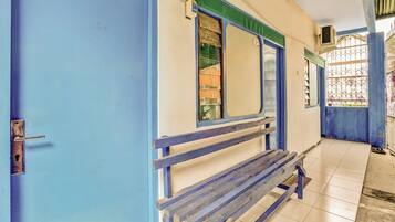 Un pasillo con una puerta azul, un banco y una ventana con reja de metal.