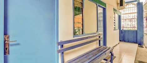 A corridor with a blue door, a bench, and a window with a metal grill.