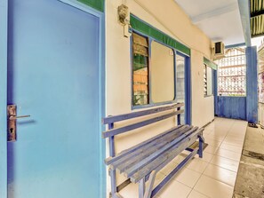 A corridor with a blue door, a bench, and a window with a metal grill. - OYO 90523 Homestay Jenggolo (Sidoarjo)