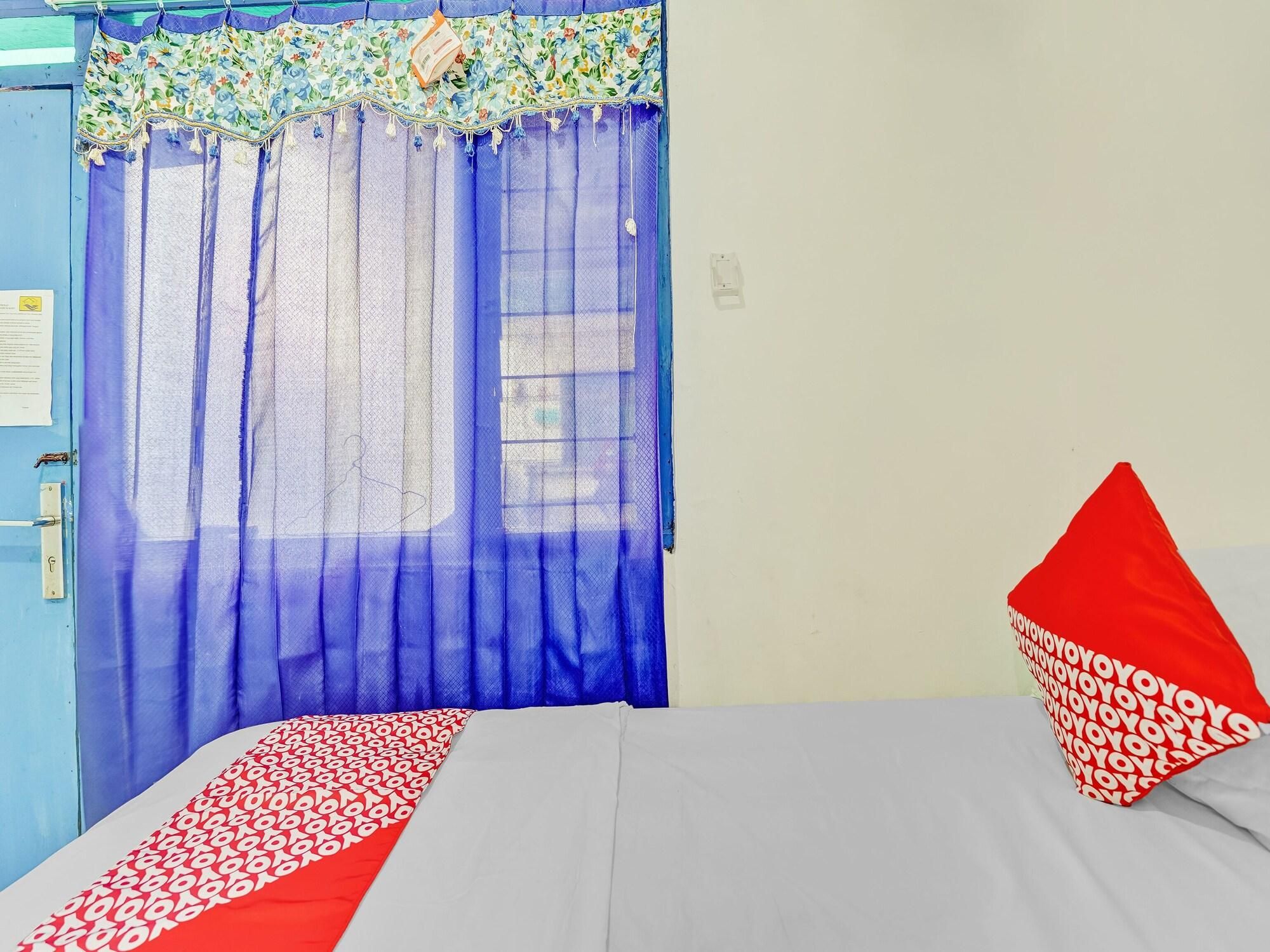 A bedroom with a bed, a window with blue curtains, and a red pillow.