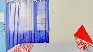 A bedroom with a bed, a window with blue curtains, and a red pillow.