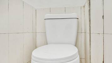 Inodoro blanco en un baño pequeño y con azulejos, con pared y suelo blancos y sin adornos.