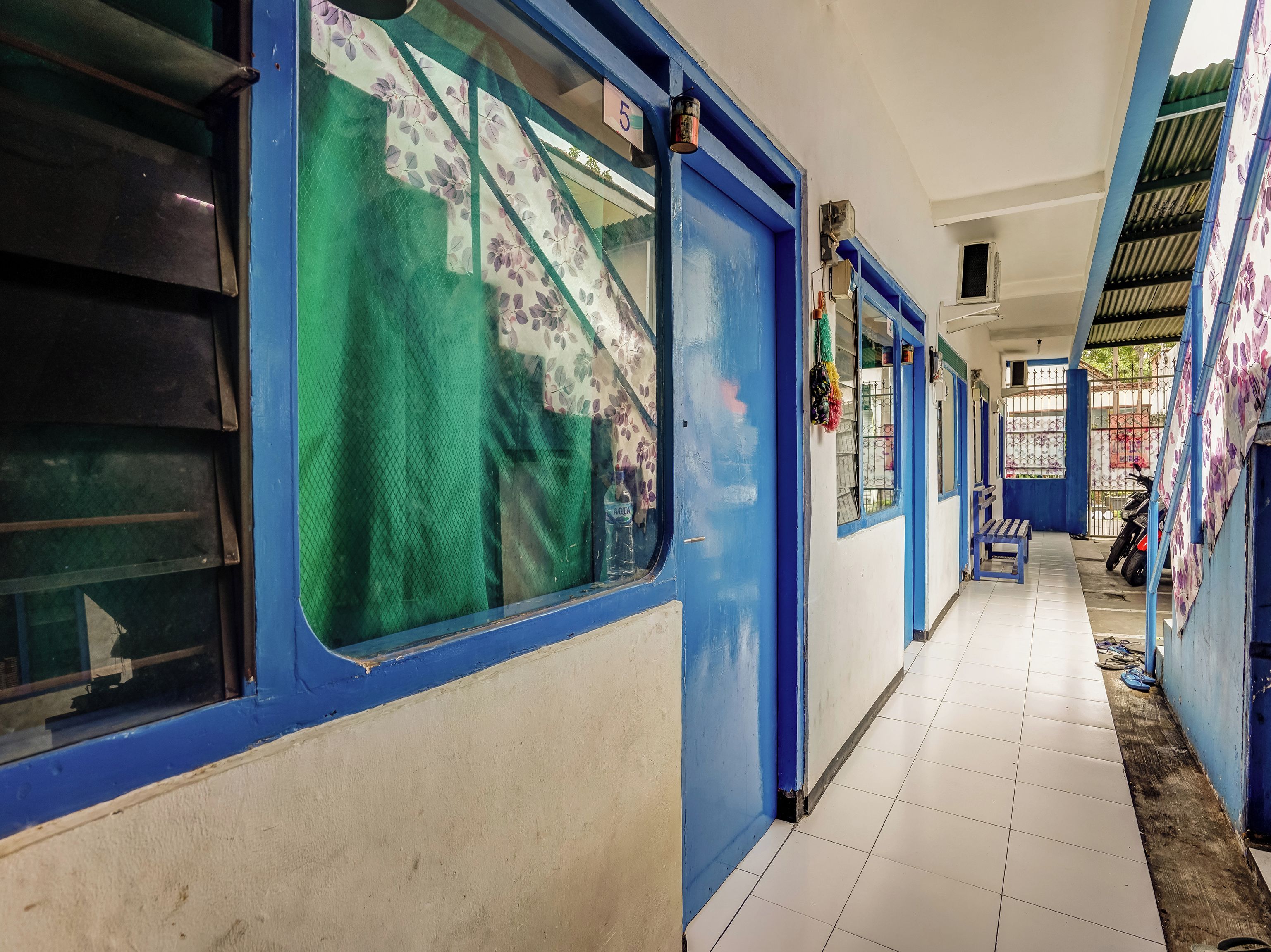 A corridor with blue doors and windows, tiled floor, and a bench.