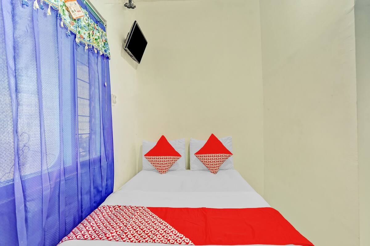 A bedroom with a bed, two pillows, a TV, and a window with blue curtains.