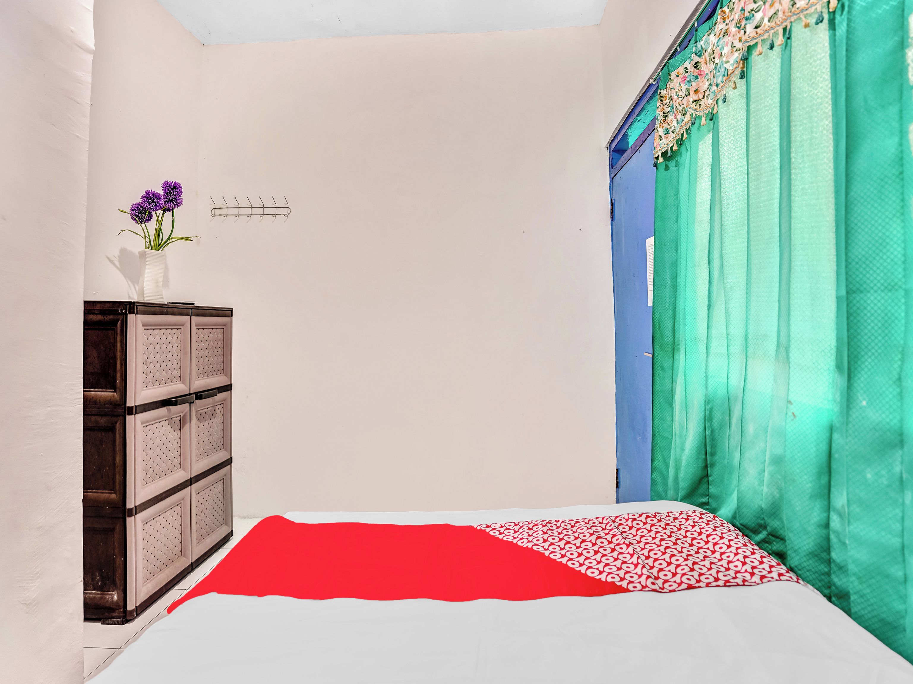 A bedroom with a bed, a dresser, a vase with flowers, and a window with curtains.