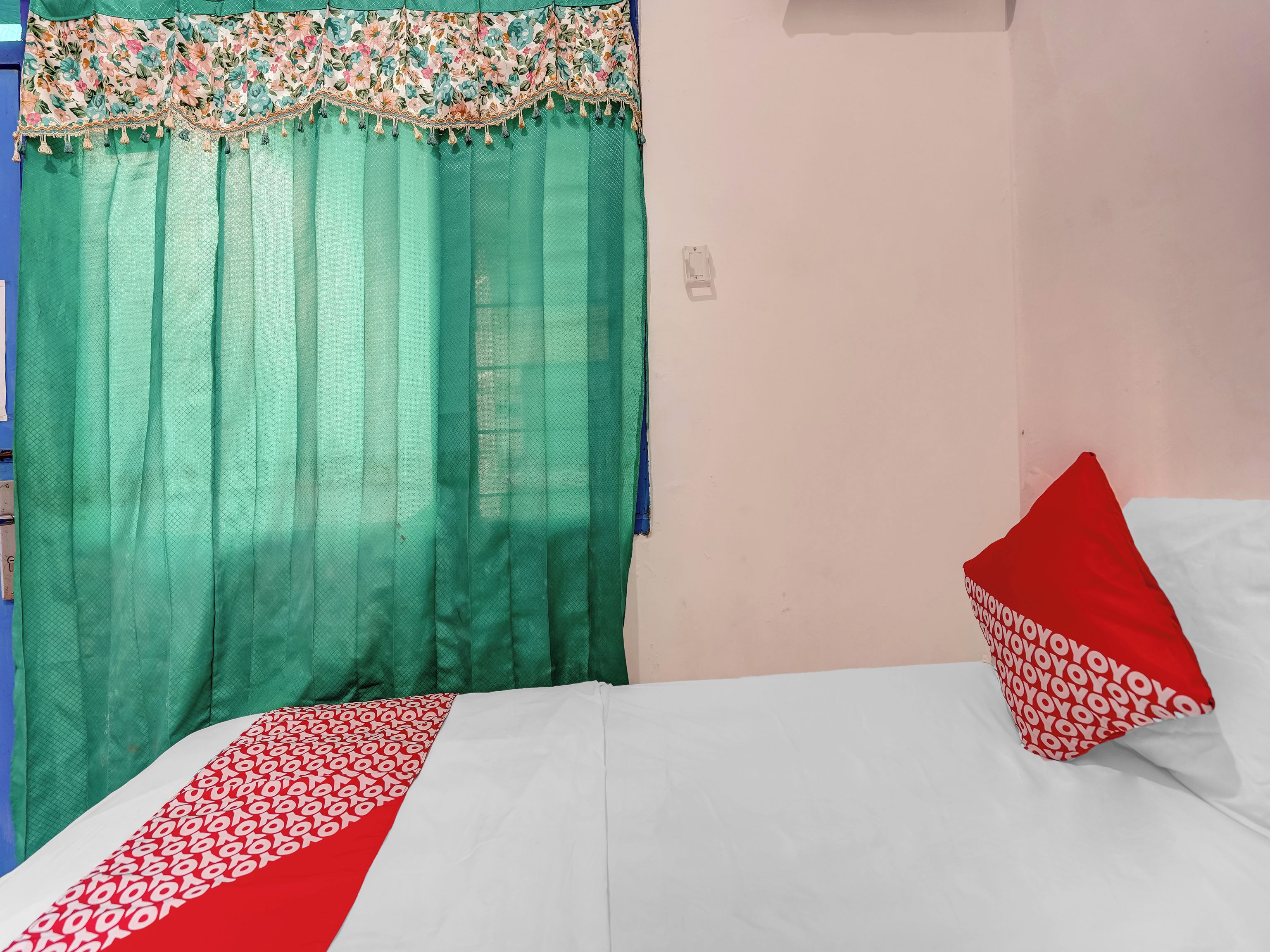 Una habitación con cama, cortina verde y almohada roja.