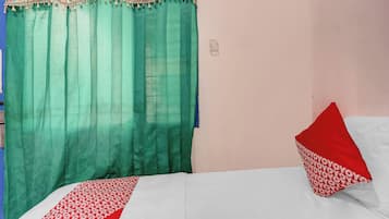 Una habitación con cama, cortina verde y almohada roja.