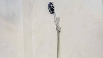 Un baño con inodoro, ducha con manguera y grifo empotrado.