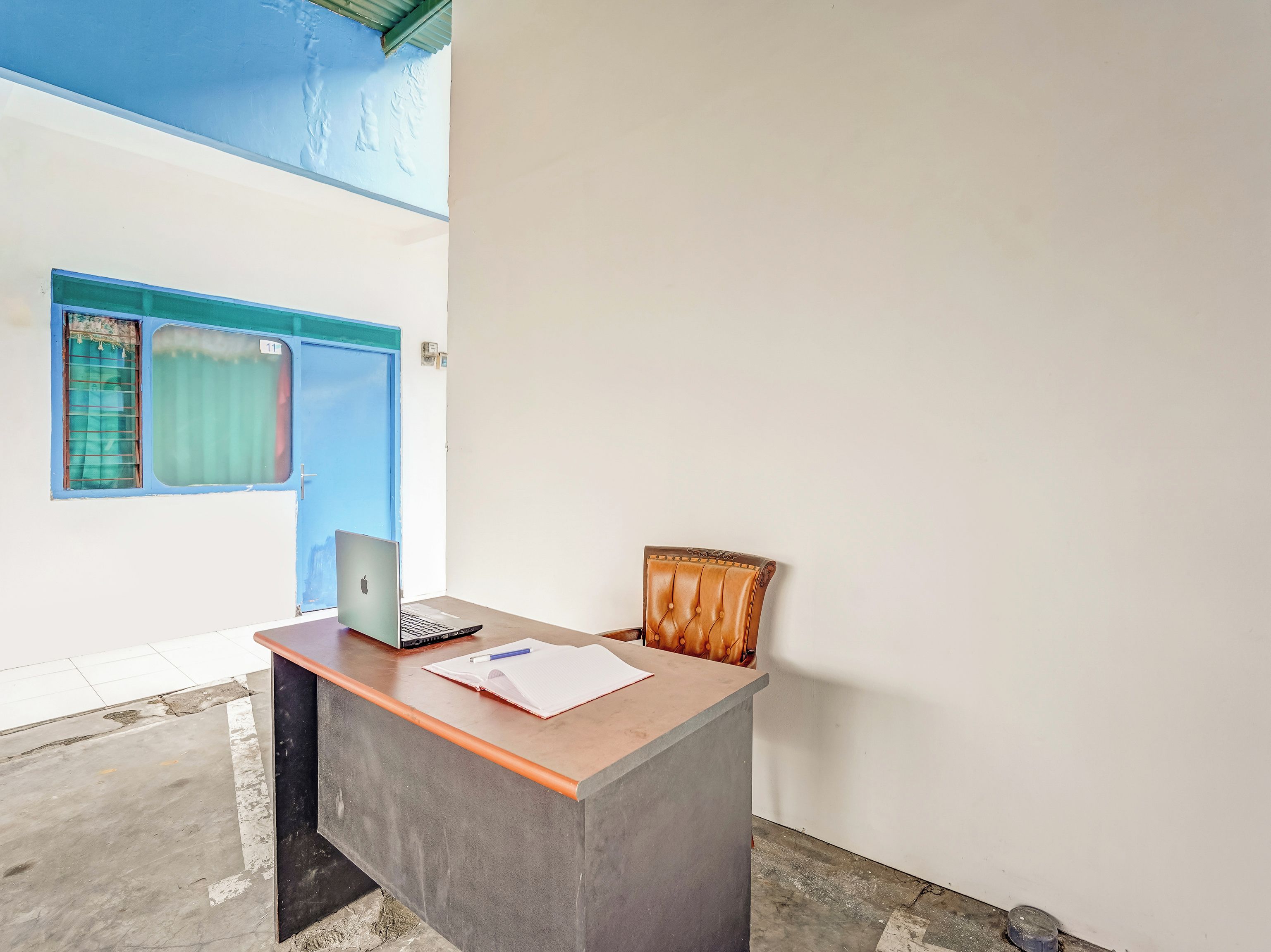 A reception desk with a laptop, a notebook, and a pen. There is a blue door and a window with curtains.