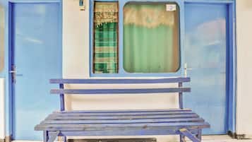 A blue bench in front of a building with two blue doors and a window with a green curtain.