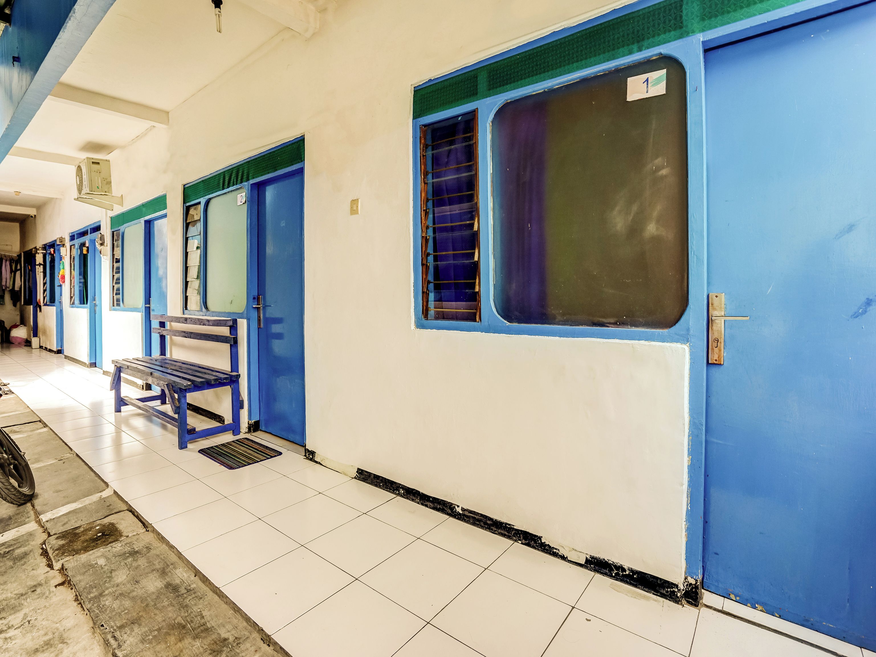Un pasillo con puertas azules, un banco y suelo de baldosas.