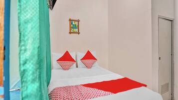 Una cama bien hecha con una colcha blanca y roja estampada, dos almohadas rojas y un libro enmarcado en la pared.