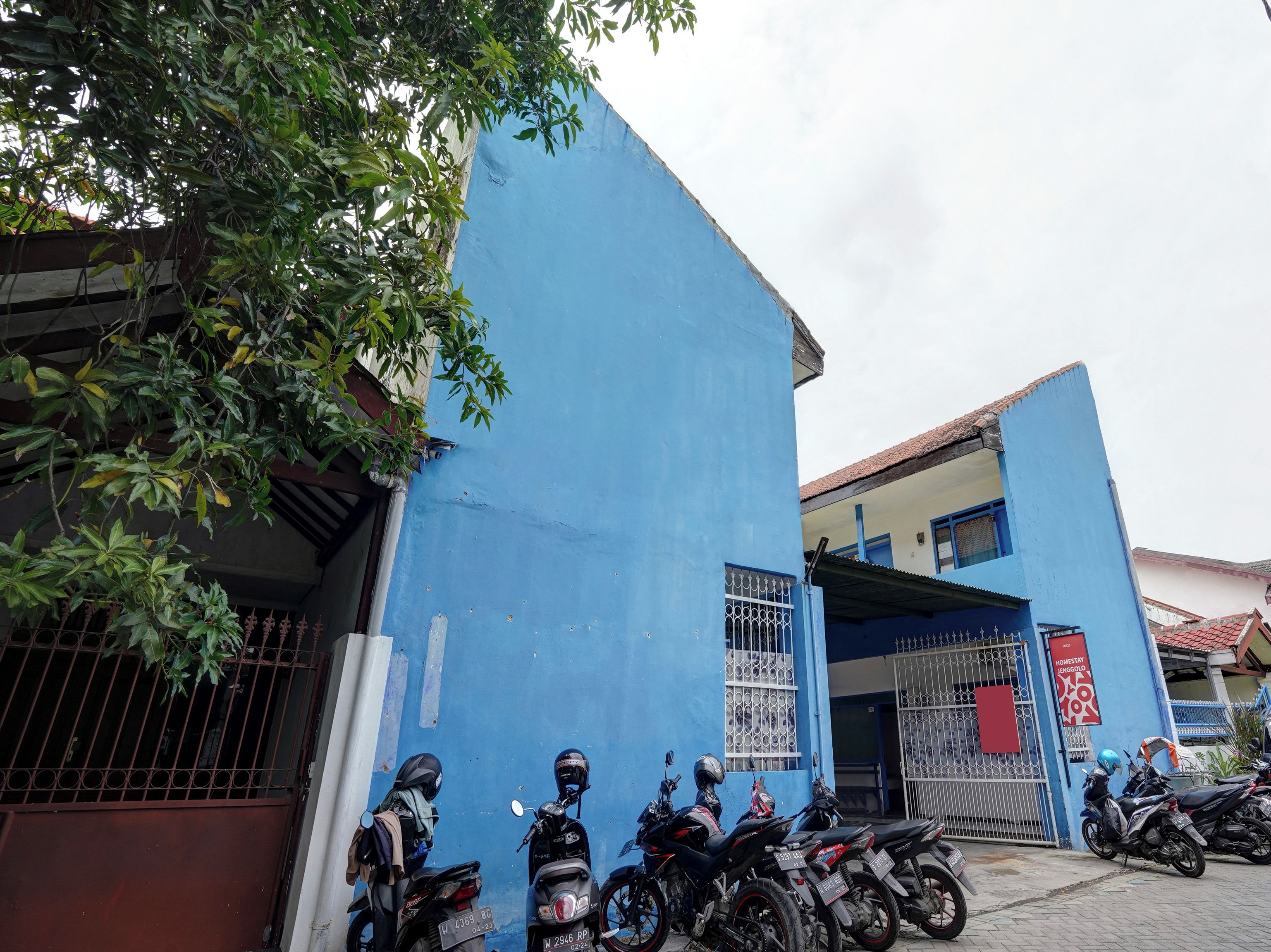 A blue building with a gated entrance, a motorcycle parked in front, and a tree partially obscuring the view.