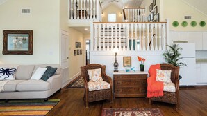 A spacious living room with a high ceiling, a staircase, and a kitchen area. - Once Upon a Tide by Ryson Vacation Rentals (Galveston)
