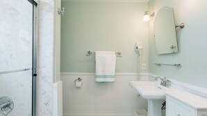 Een badkamer met een douche, wastafel, spiegel en handdoekhouder.