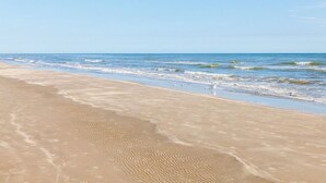 A sandy beach with gentle waves and a clear sky. - Once Upon a Tide by Ryson Vacation Rentals (Galveston)