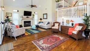 A spacious living room with a fireplace, a staircase, and a balcony. - Once Upon a Tide by Ryson Vacation Rentals (Galveston)