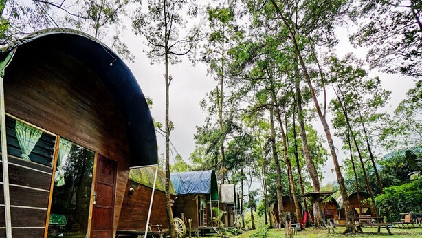 A rustic cabin-style accommodation with a large wooden structure, a covered porch, and a pathway leading through a garden. - OYO 90474 Caravan Camp (Batu)