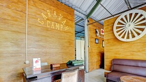 A reception area with a wooden desk, a brown leather sofa, and a large wooden wheel decoration. - OYO 90474 Caravan Camp (Batu)