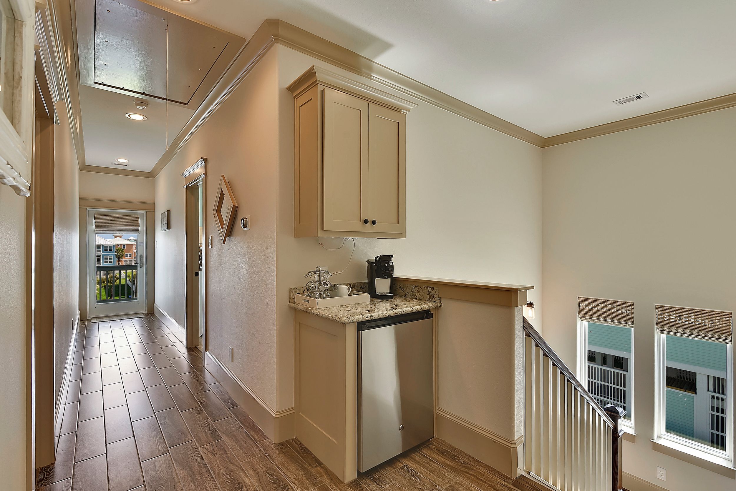 A hallway with a kitchen area, including a refrigerator, a coffee maker, and a window with blinds.