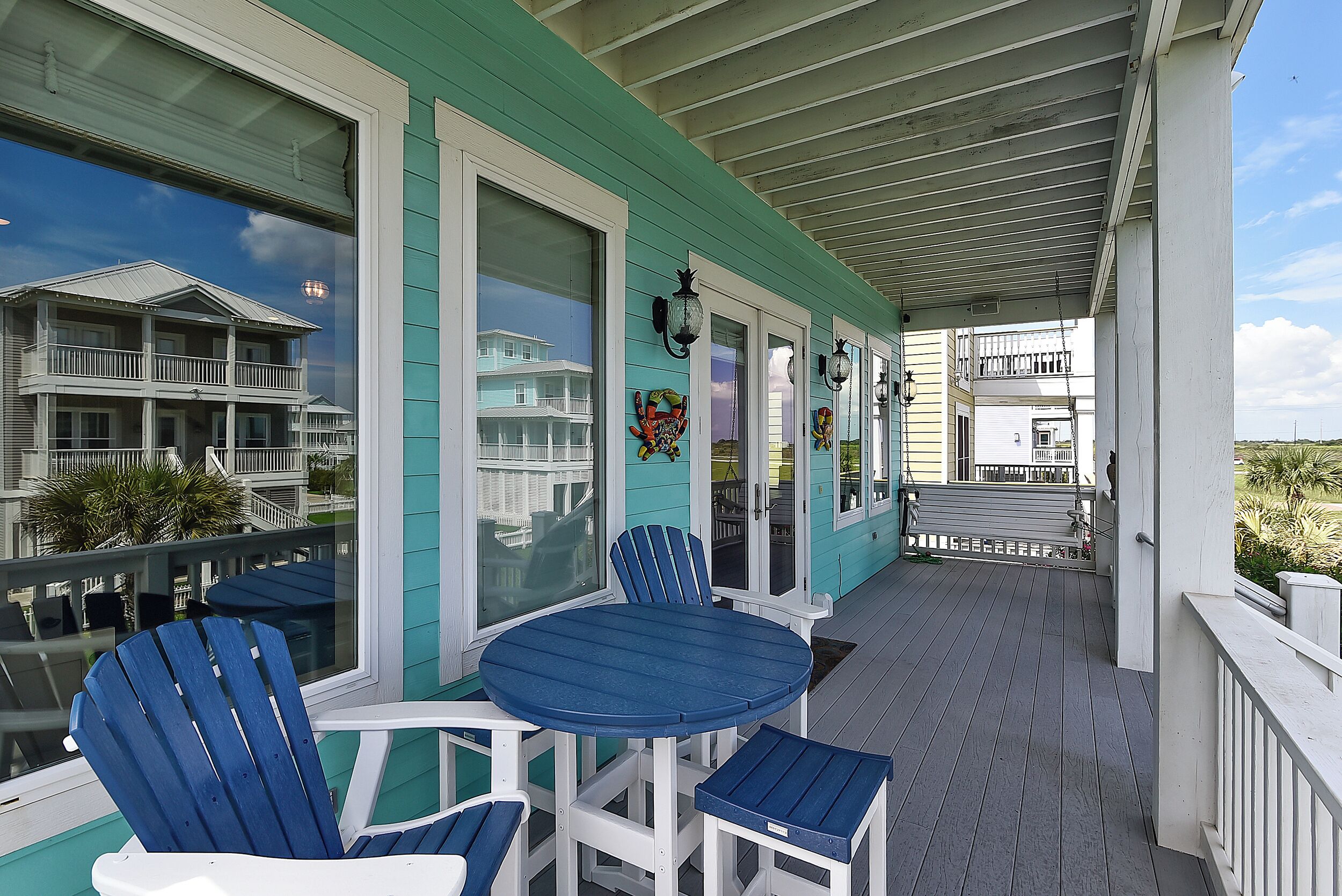 A covered porch with a round table and two blue Adirondack chairs.