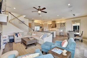 A spacious living area with a sofa, ottoman, and coffee table, a staircase with a railing, and a kitchen in the background.