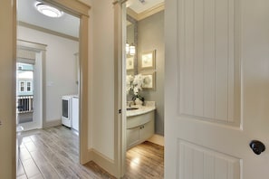 A bathroom with a sink, mirror, and vanity. There is a door leading to another room. - Neptune's Sanctuary by Ryson Vacation Rentals (Galveston)