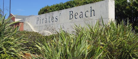A sign reading "Pirates' Beach" with surrounding greenery and a building in the background.